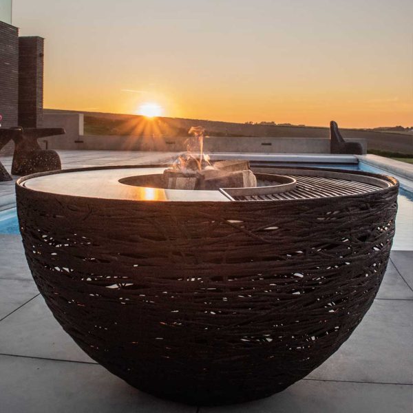 Image of last glimpse of sun disappearing behind hill with black-colored Lava Nest barbecue and firepit in foreground by Unknown Nordic Furniture
