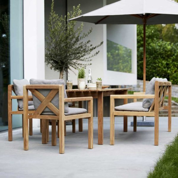 Image of Grace teak garden dining furniture by Cane-line, shown on minimalist poured concrete terrace with olive tree in background