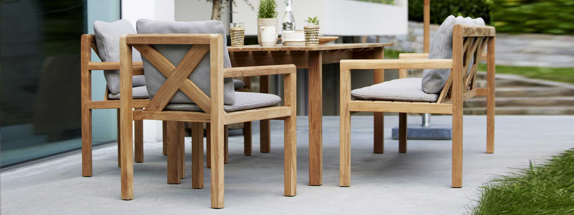 Image of Grace teak table, benches and chairs by Cane-line, showing the furniture with light grey cushions