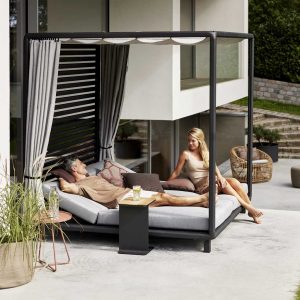 Image of couple lying down relaxing inside Laze daybed with ceiling by Cane-line garden furniture