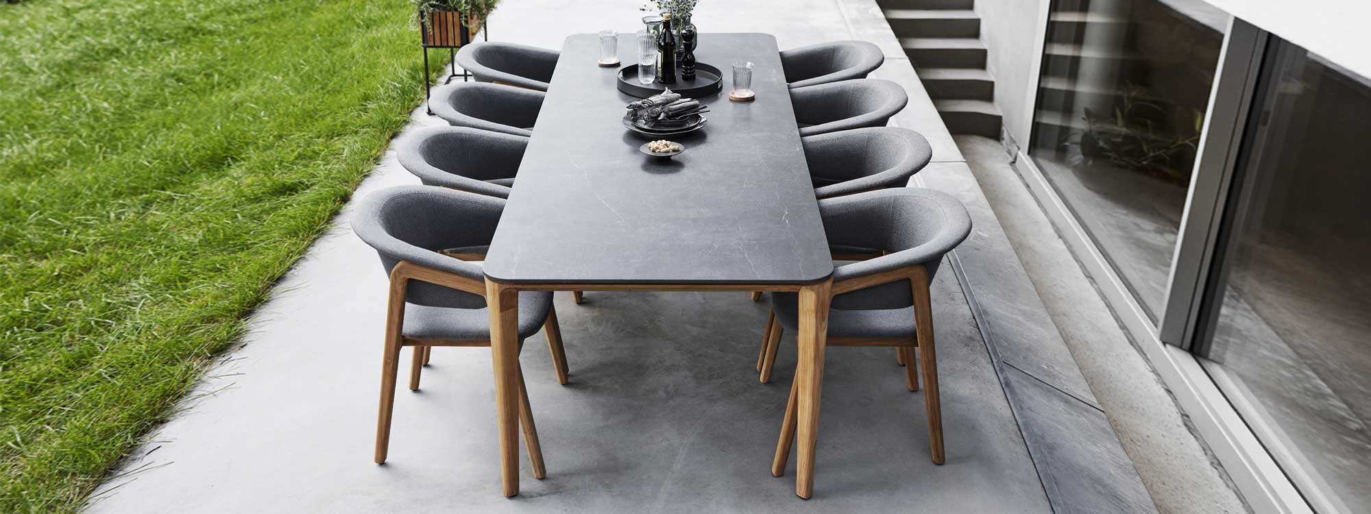 Image of Aspect teak dining table with black ceramic top and Luna teak garden chairs by Cane-line on poured concrete terrace