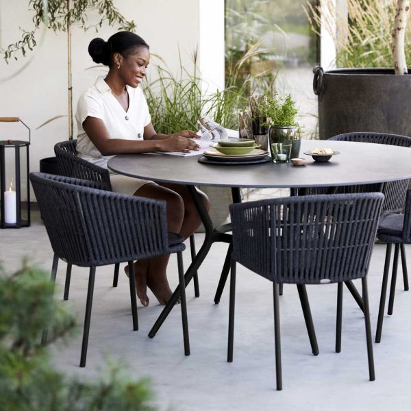 Image of Joy round garden table and dark grey Moments dining chairs by Cane-line