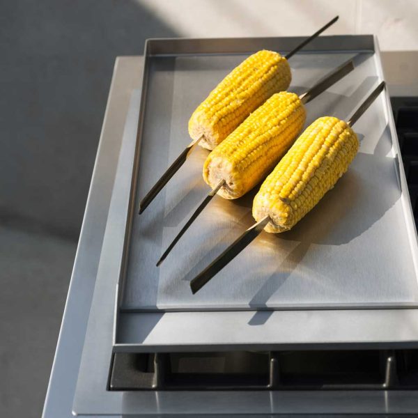 Image of 3 skewered corn cobs on top of Norma outdoor kitchen's stainless steel teppanyaki by RODA
