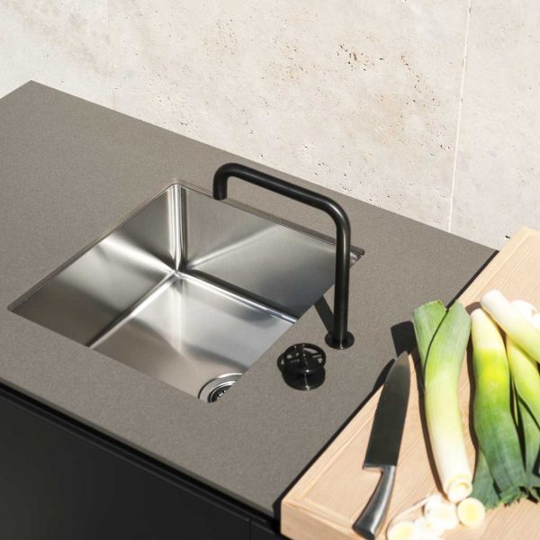 Image of detail of RODA Norma outdoor stainless steel sink unit with ceramic work surfaces and larch chopping board with leeks on top