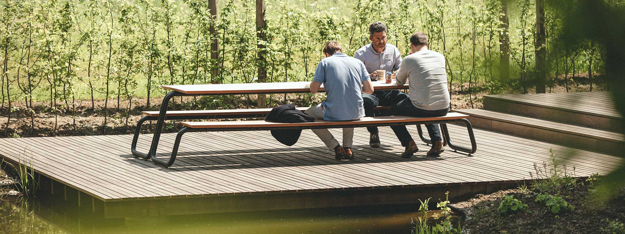 Image of The Table modern picnic table and integrated benches with tubular steel frame and afzelia hardwood surfaces, shown on raised wooden decking