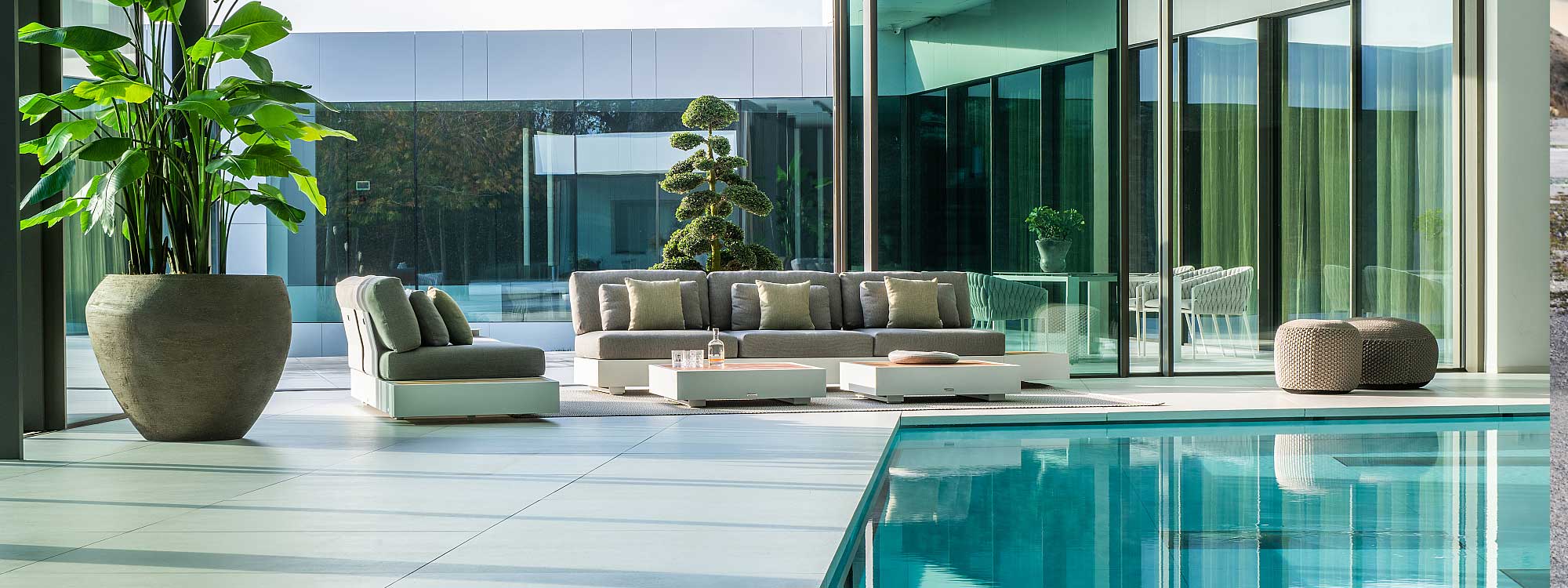 Image of pair of white Bari luxury garden sofas on indoor poolside with Fortuna Socks dining chairs and Vigo XL extending garden table on the terrace outside