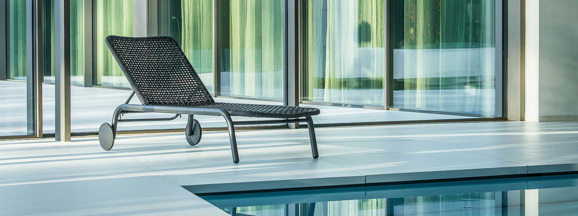 Image of Durham sun lounger with tubular aluminium frame and charcoal coloured Polyolefin rope seat and back, shown on minimalist poolside with floor to ceiling glass in background