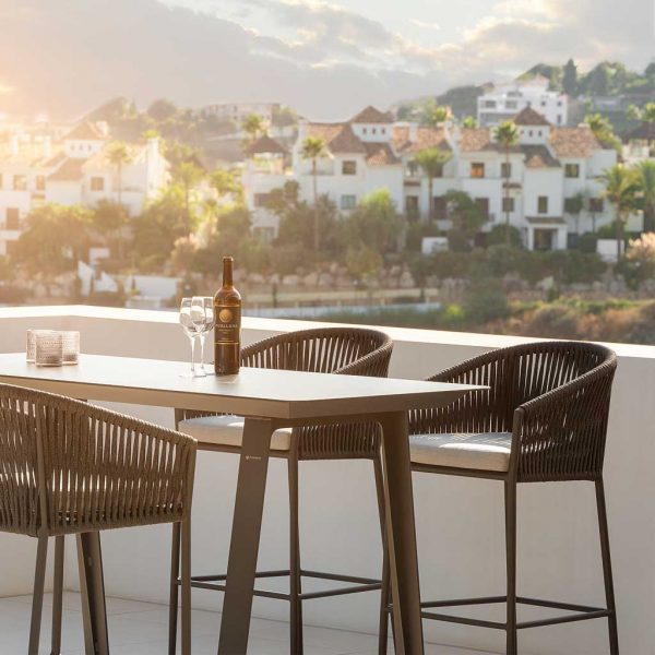 Image of Fortuna Rope black tub bar stools on a white-washed terrace at dusk, with houses on a hillside in the distance