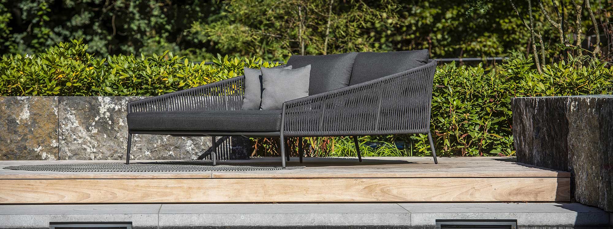 Image of charcoal black Fortuna Rope twin garden daybed on terrace with shrubs in background