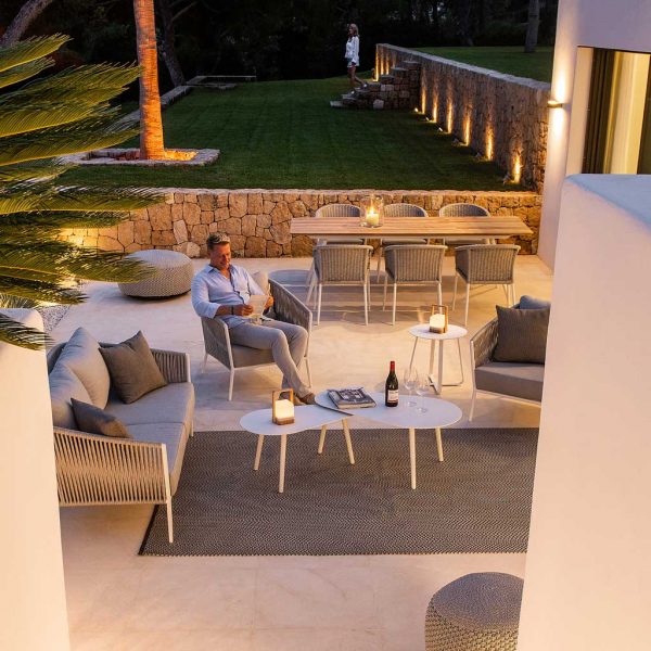 Image of man sat on Fortuna Rope garden lounge chair at night, reading a book on illuminated terrace