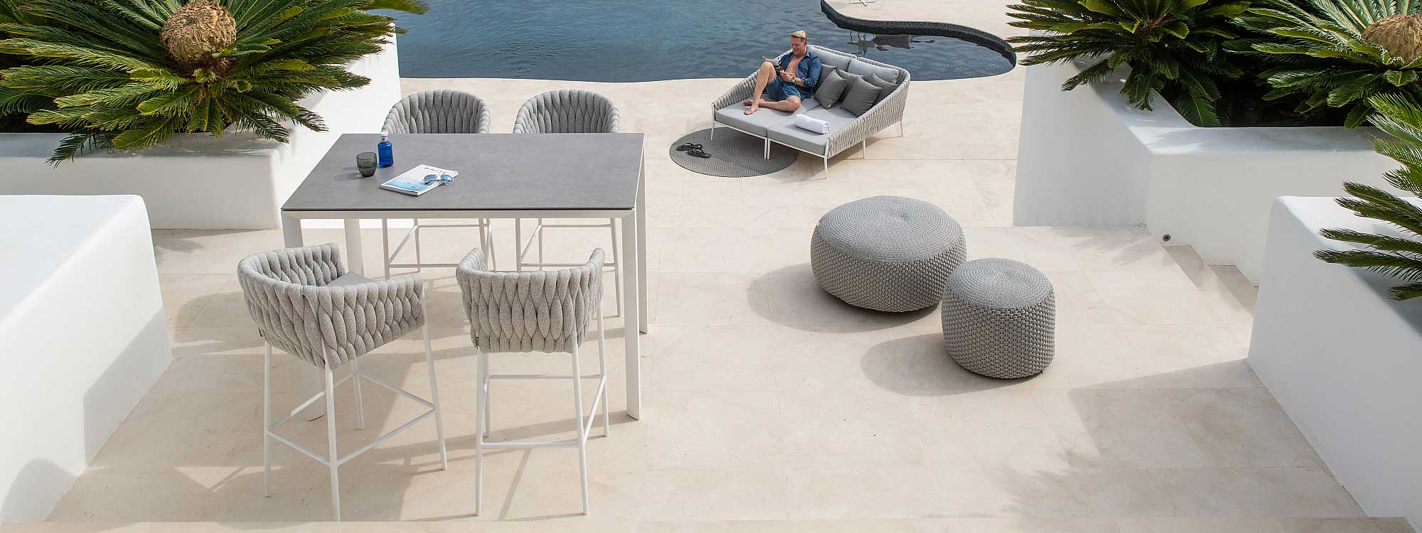 Image of Fortuna Socks outdoor bar stools and daybed on sunny poolside, surrounded by white-washed raised flower beds filled with architectural palms