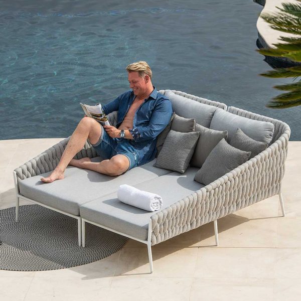 Image of man lying back and reading on Fortuna Socks modern garden daybed by Jati & Kebon, shown on sunny poolside