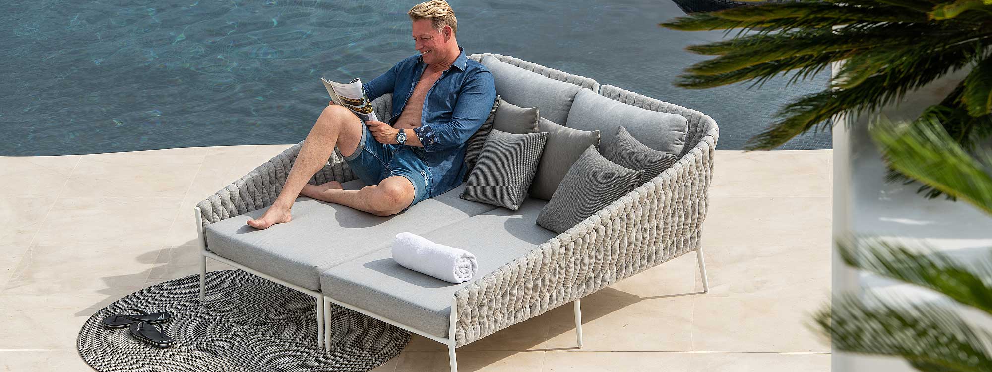 Image of man smiling whilst reading on Fortuna Socks daybed in white aluminium with light-grey woven socks back