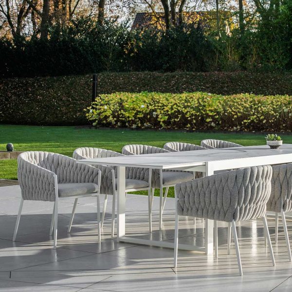 Image of Fortuna Socks white garden dining chairs with Jati & Kebon large garden table on terrace, with lawn and beech hedges in the background