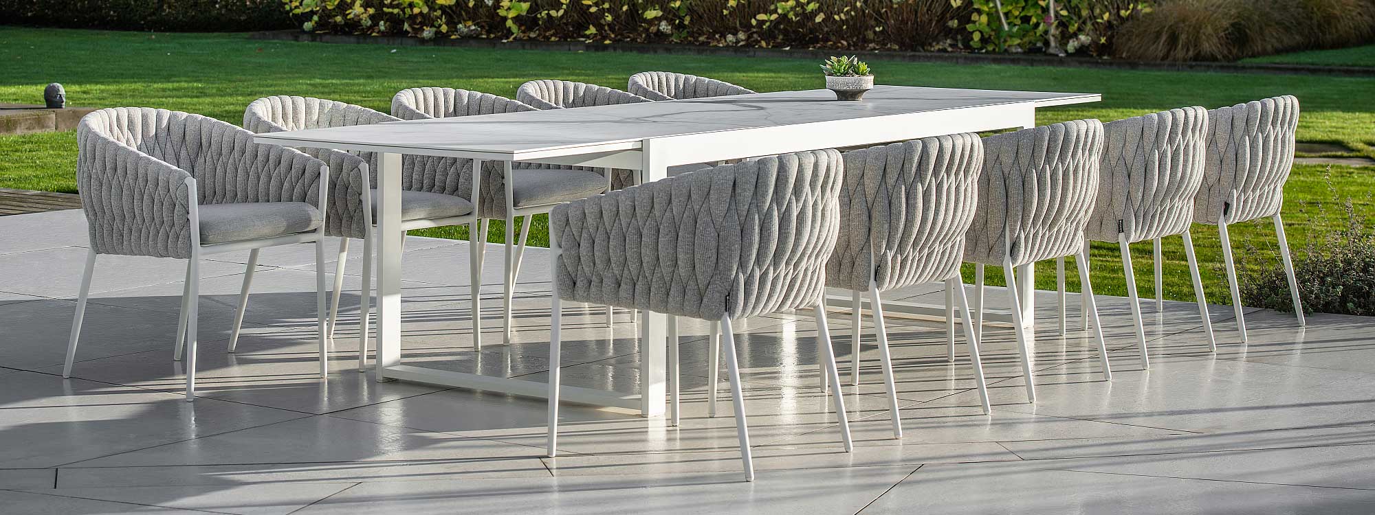 Image of white-grey Fortuna Socks with Vigo XL extending garden table on terrace, with lawn and shrubs in background