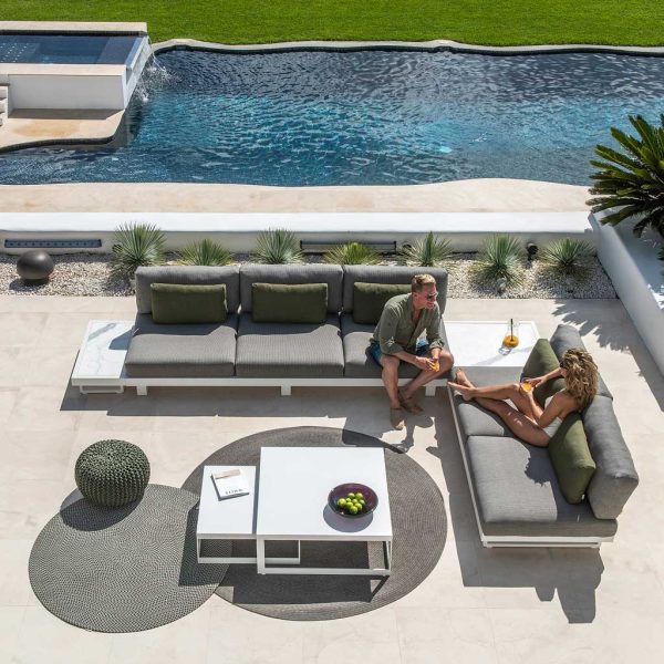 Image of aerial view of man and woman chatting on Fano modern outdoor corner sofa, with azure water of swimming pool in the background