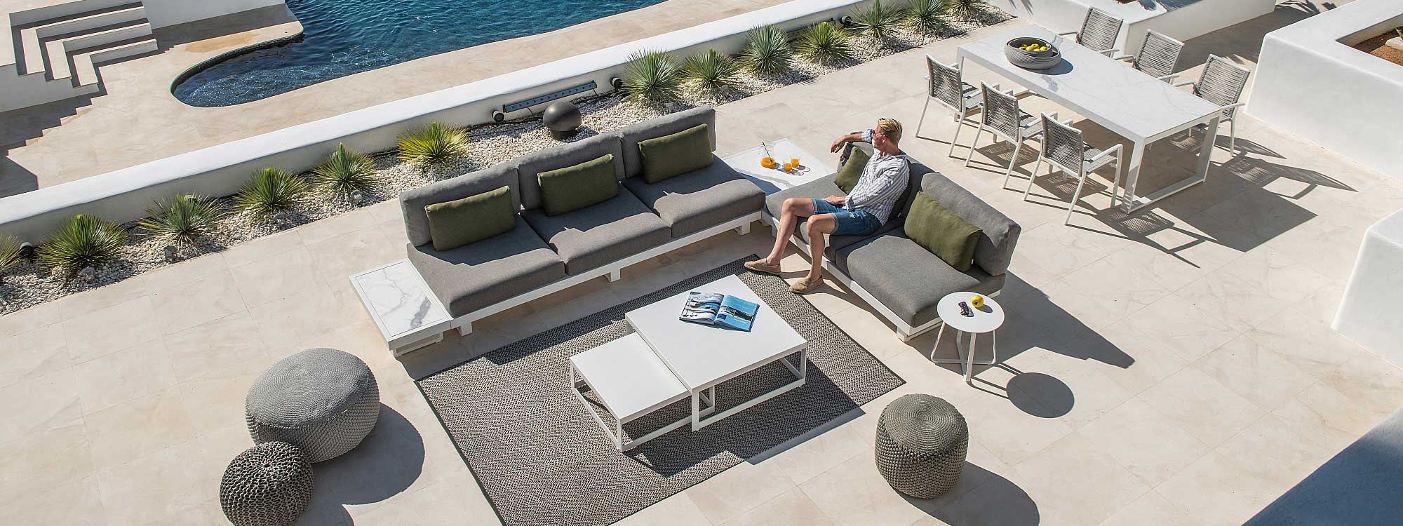 Image of man sat on Fano modern white garden sofa, shown with white grey cushions and graduario ceramic table tops