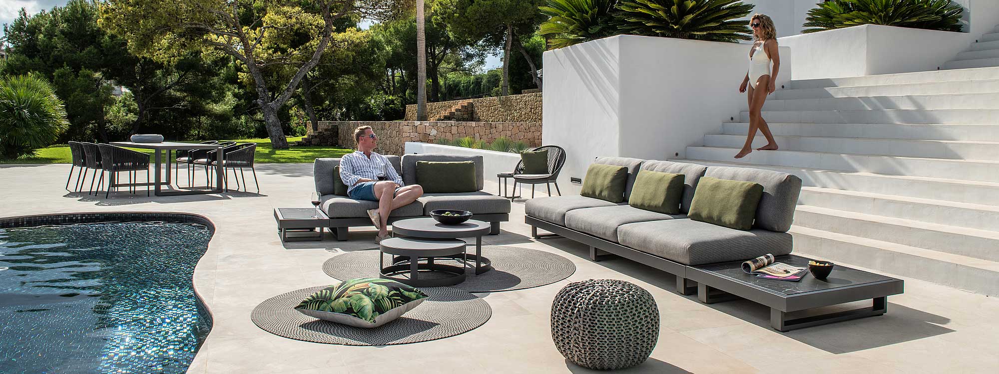 Image of Fano dark grey garden sofa with grey cushions and dark marble ceramic table tops on sunny poolside