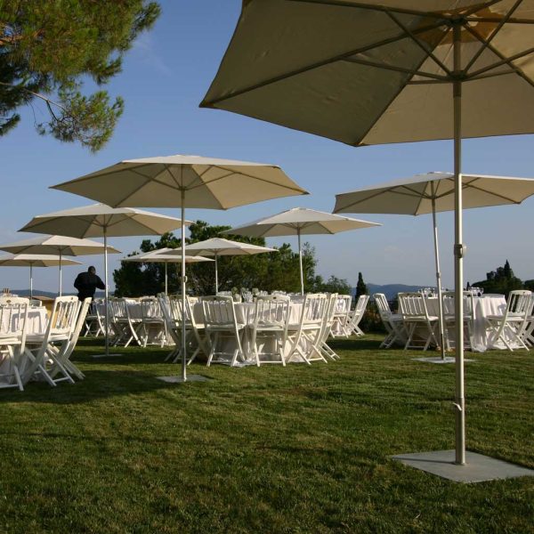 Image of multiple P50 small mast parasols over event furniture on grassy lawn