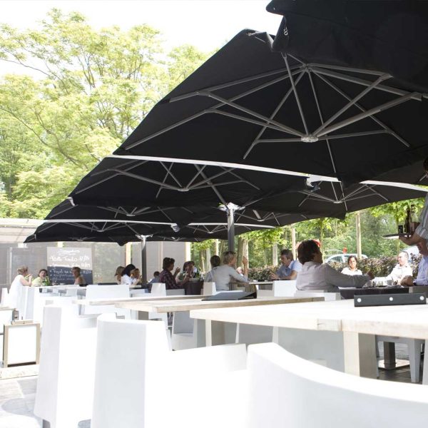 Image of Prostor P6 parasol with 4 black canopies and white dining furniture beneath