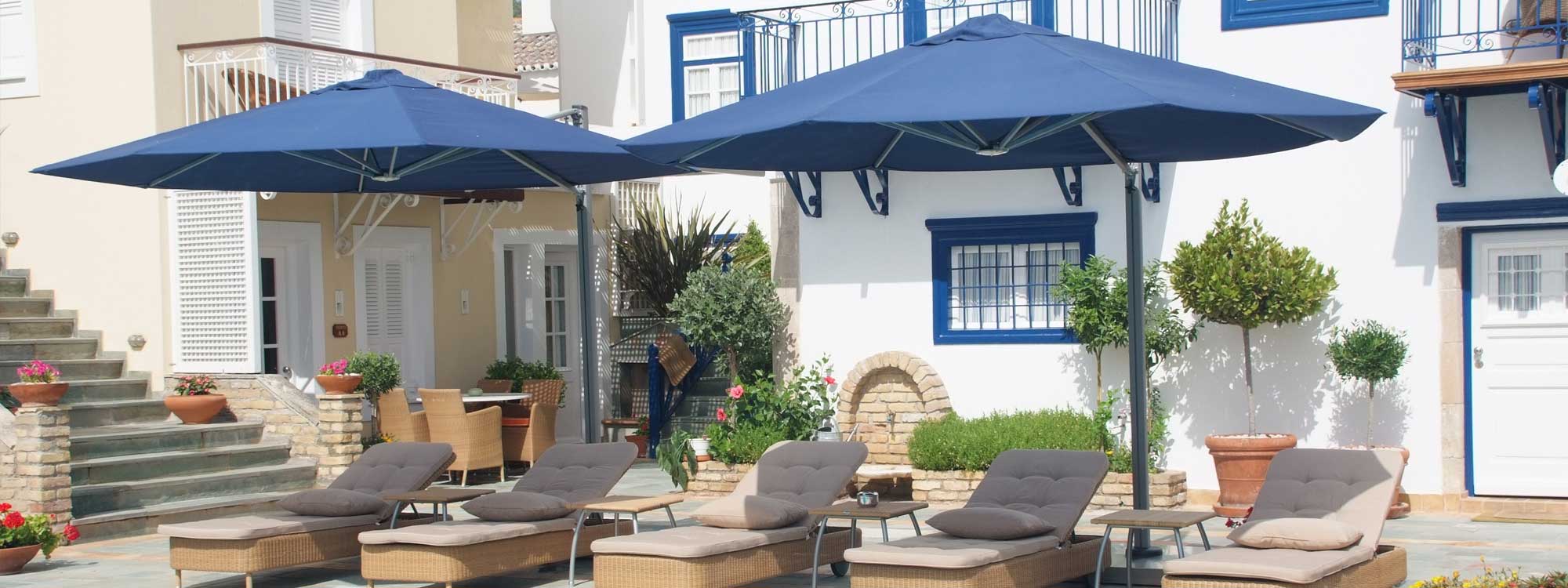 Image of pair of Prostor P7 blue side post parasols above 4 sun loungers on a sunny poolside