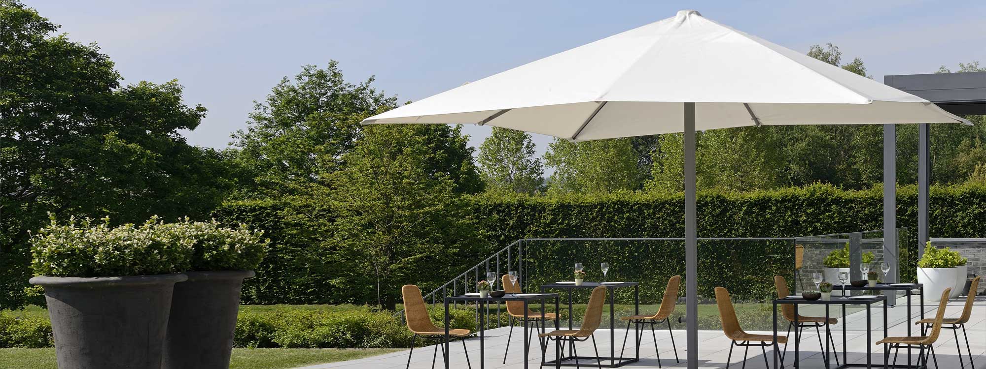 Image of Prostor P8 large square centre pole parasol opened above bistro furniture on sunny terrace