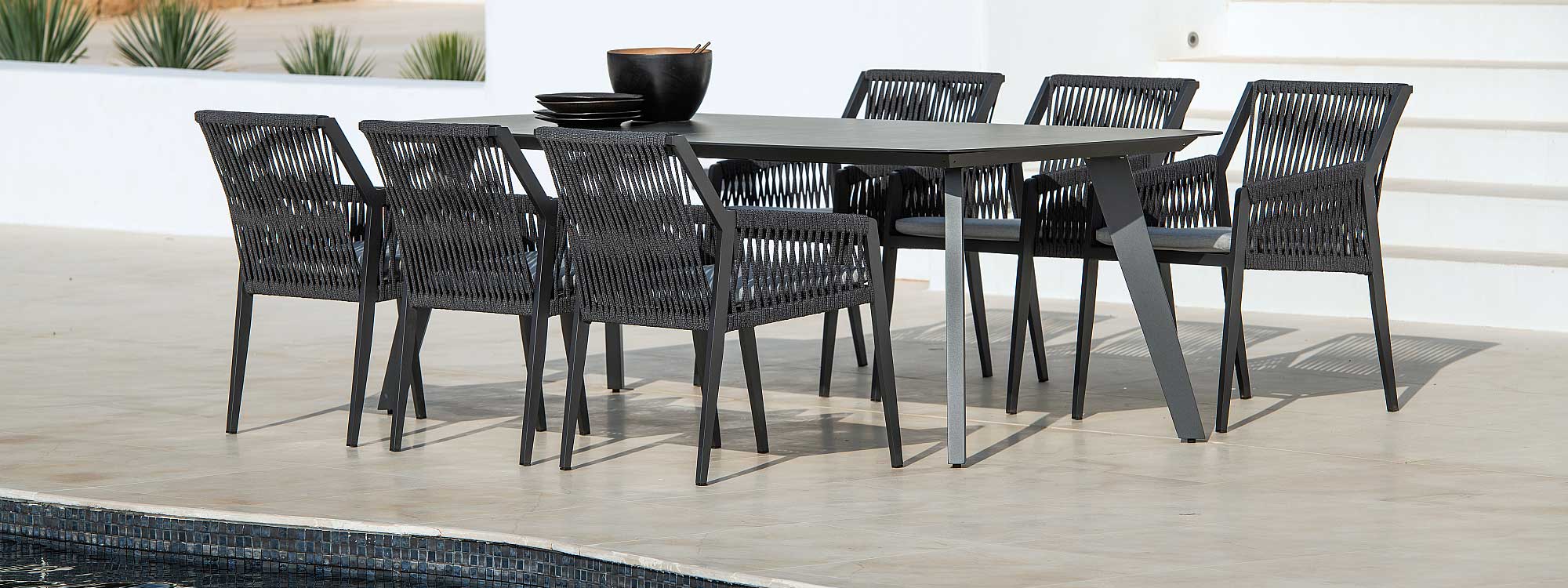 Image of Ritz garden table with tapered black legs and dark marble table top, surrounded by Ritz contemporary carver chairs on sunny poolside