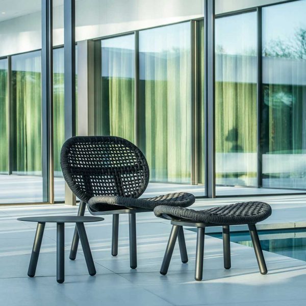 Image of Skate contemporary garden chair and foot rest with black tubular aluminium frames and black woven polyolefin surfaces, shown on sleek modern terrace