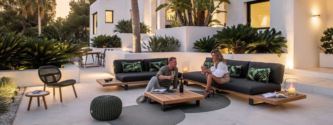 Image of white-washed terrace at dusk with couple enjoying a drink on Truro Lounge teak and aluminium corner sofa by Jati & Kebon