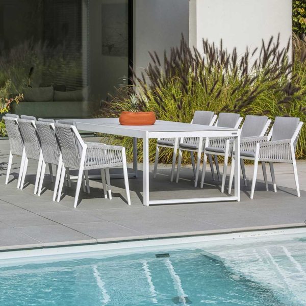Image of Vigo XL white extending garden table with cement grey ceramic top, together with Ritz white dining chairs with light-grey cushions, shown in sunny poolside