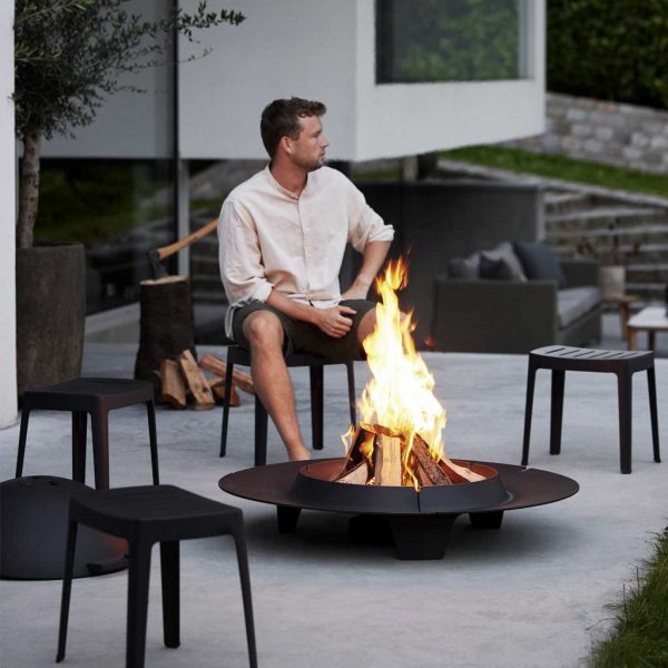 Image of man sat on Cut stool seat in front of Ember fire pit by Cane-line