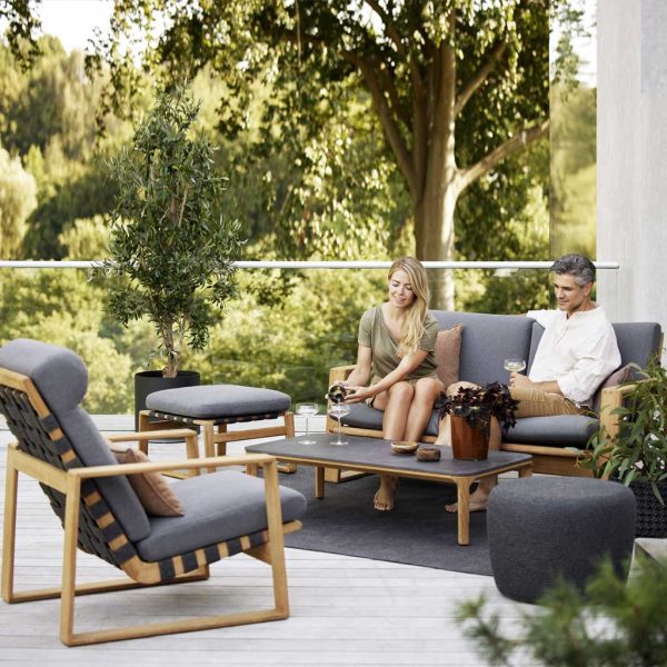 Image of couple sat on Endless Soft outdoor lounge set by Cane-line, shown on terrace with trees in background