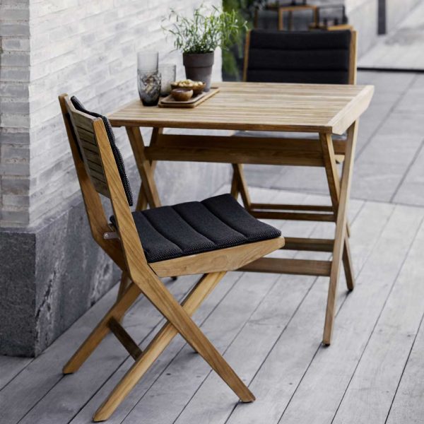 Image of pair of Cane-line Flip teak chairs with dark grey Focus fabric cushions next to Flip folding teak table