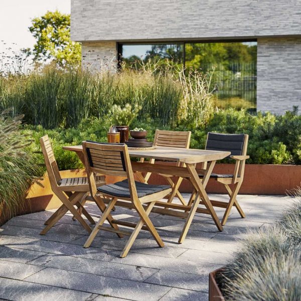 Image of 4 Cane-line Flip teak chairs with grey cushions around Flip folding teak table, with architectural grasses in background