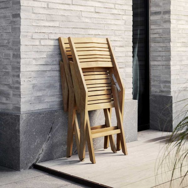 Image of pair of folded Cane-line Flip teak chairs, leaning against a stone wall.