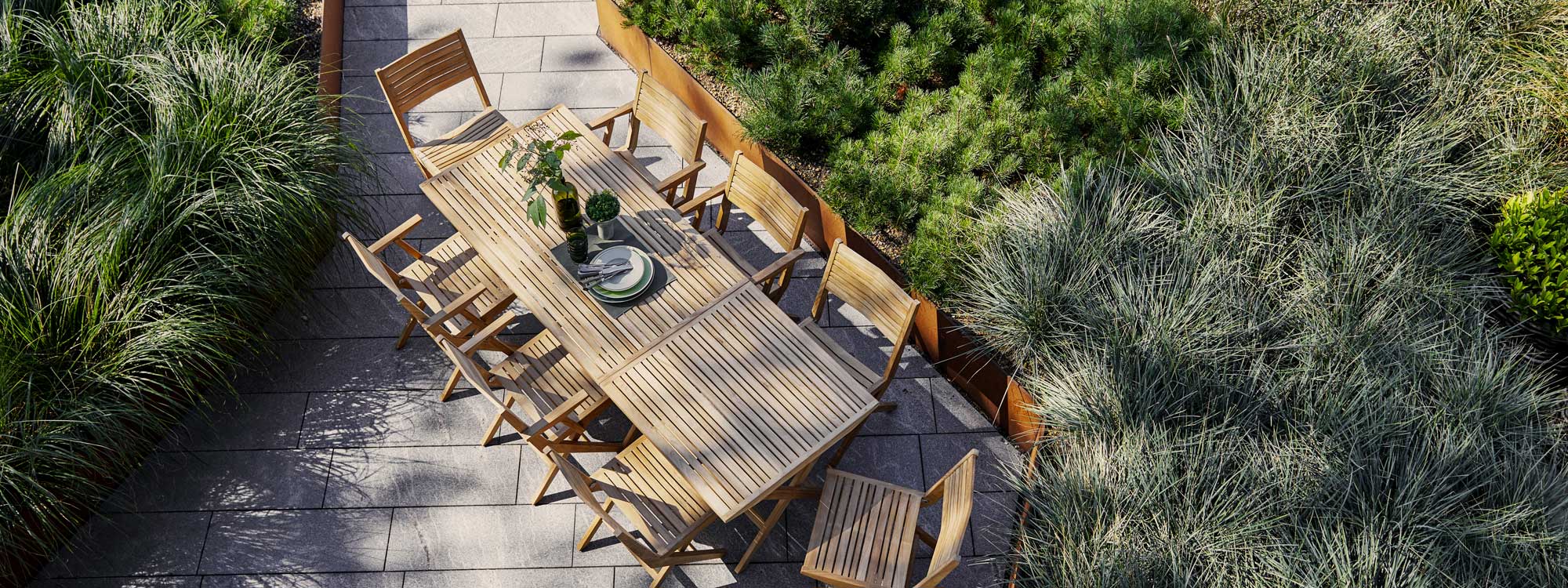 Image of pair of Cane-line Flip tables next to one another, surrounded by Flip folding teak garden chairs, surrounded by raised beds of grasses