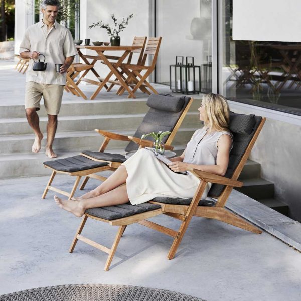 Image of women with her feet up, sat on Flip teak Steamer chair, with Flip folding dining furniture in background by Caneline furniture company.