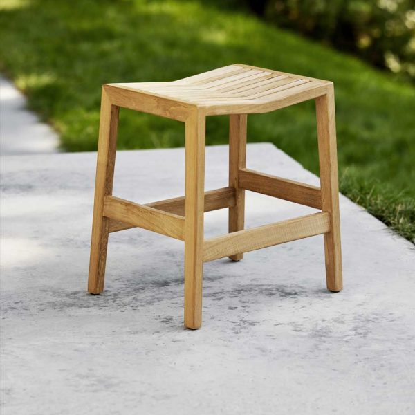 Image of Flip teak stool seat by Caneline, shown on terrace with grass in background