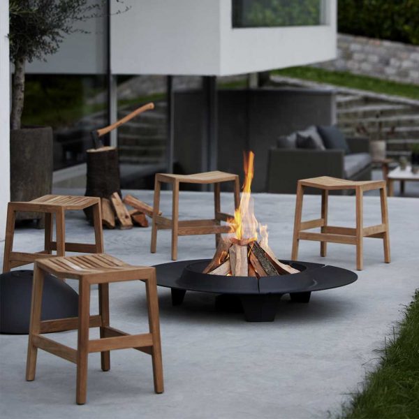 Image of Cane-line Ember fire pit, surrounded by Flip teak stools on minimalist terrace at dusk