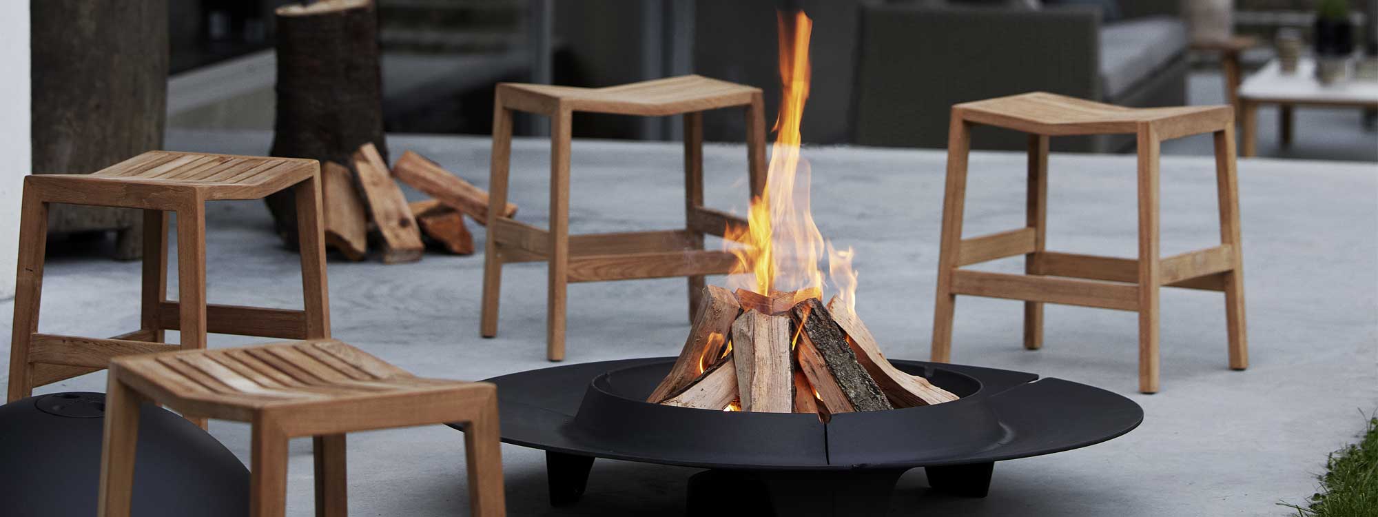 Image of Flip teak stool seats around Ember fire pit by Cane-line