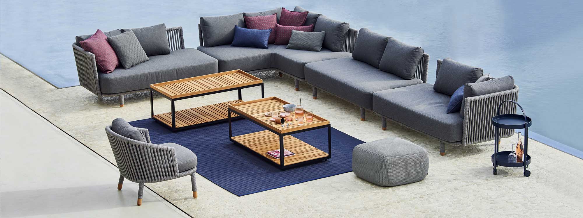 Image of pair of rectangular Cane-line Level coffee tables with teak tops, surrounded by large Moments grey corner sofa