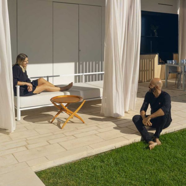 Image of woman lying on Oiside 45 minimalist garden sofa whilst chatting to a man sat on a sunny terrace