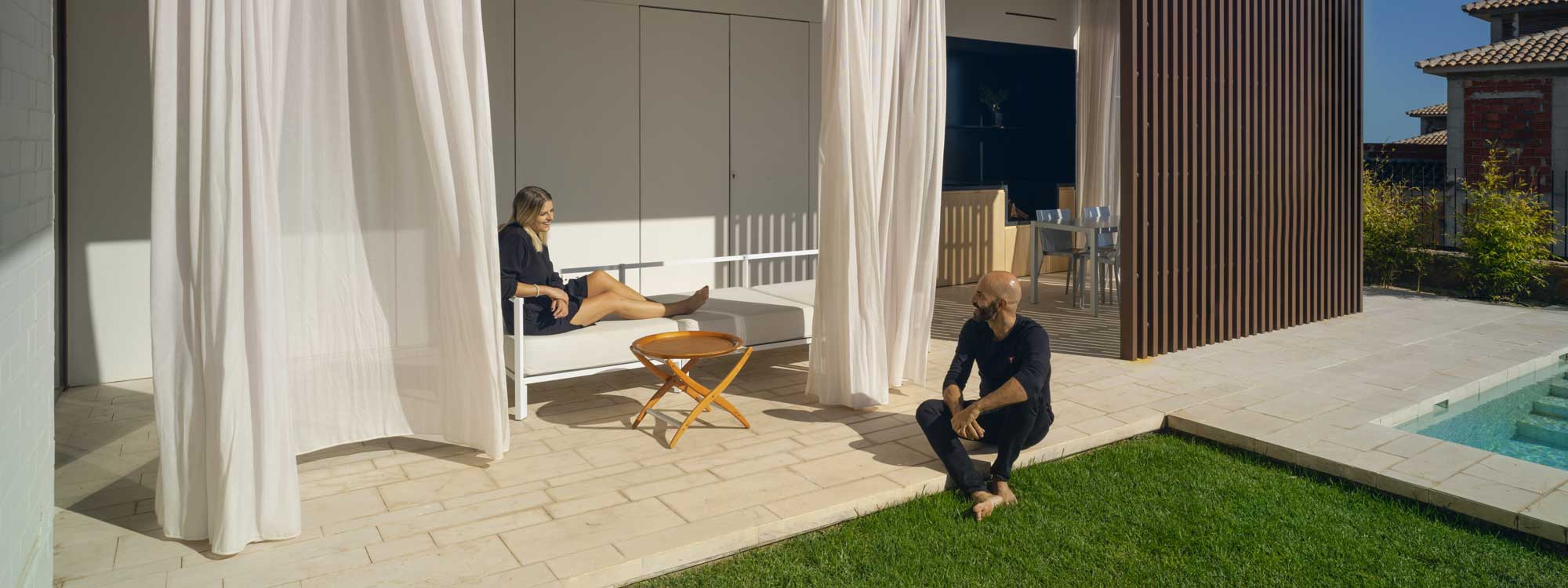 Image of woman sat on Oiside 45 modern garden sofa whilst chatting to a man sat on sunny terrace