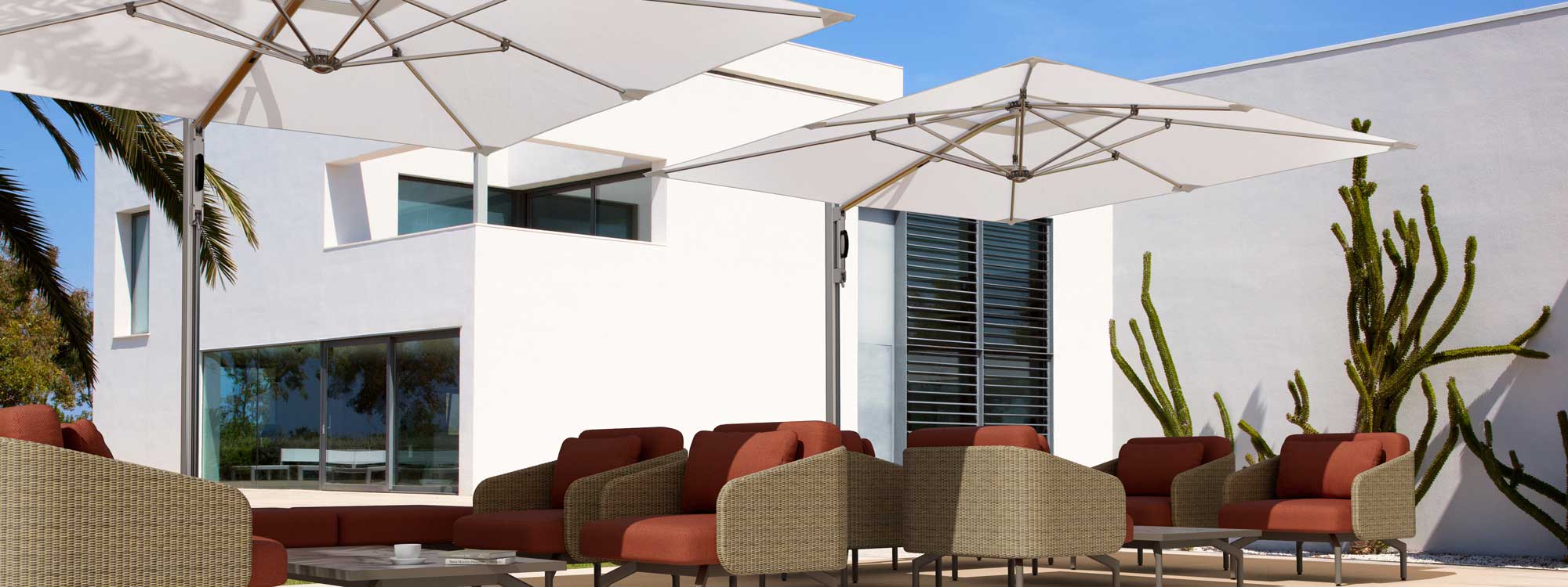 Image of Tuuci Ocean Master white cantilever parasols with polished titanium mast and ribs, with lounge furniture beneath and whitewashed building and large cactus in background