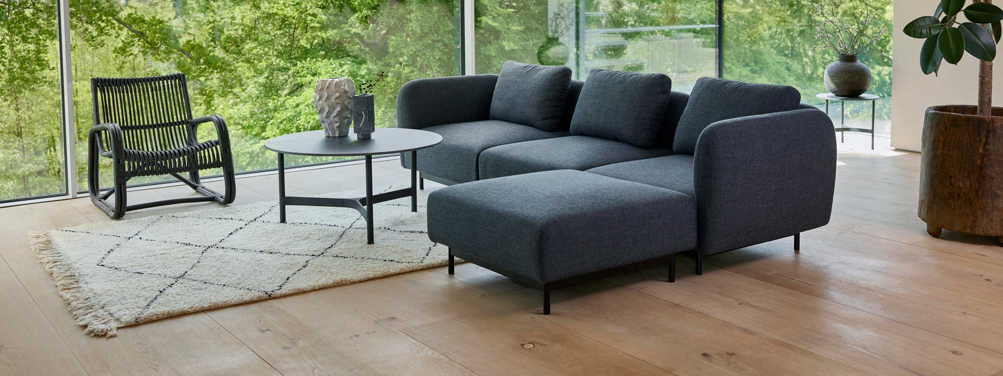 Image of Aura modern sofa and footrest in dark-grey Cane-line Ambiance fabric, with Twist circular ceramic coffee table in the centre