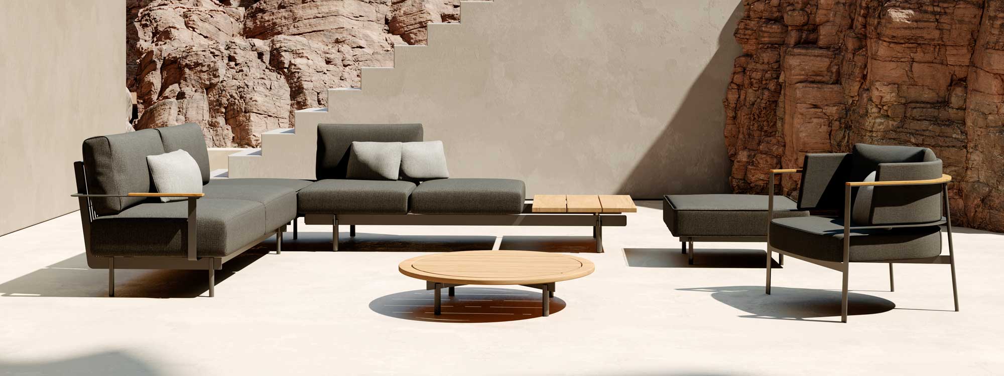 Image of modular configuration of Oiside Penda minimalist garden sofa and lounge chair, together with circular low table shown on hot terrace with rockface in the background