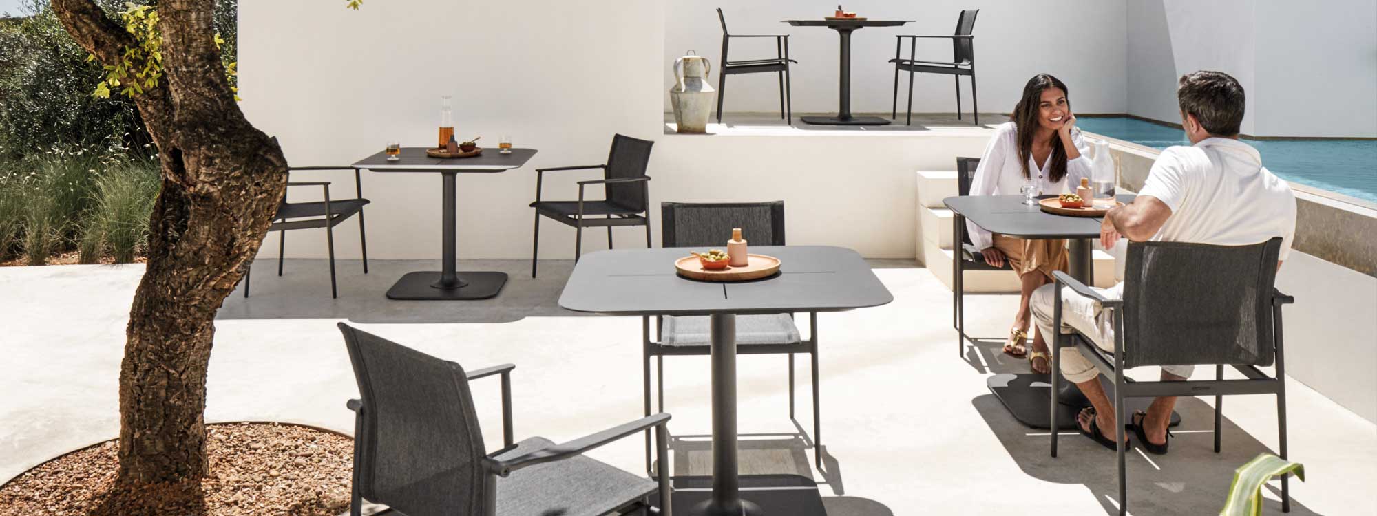 Image of 180 modern garden chairs and Grid bistro tables by Gloster in sunny courtyard