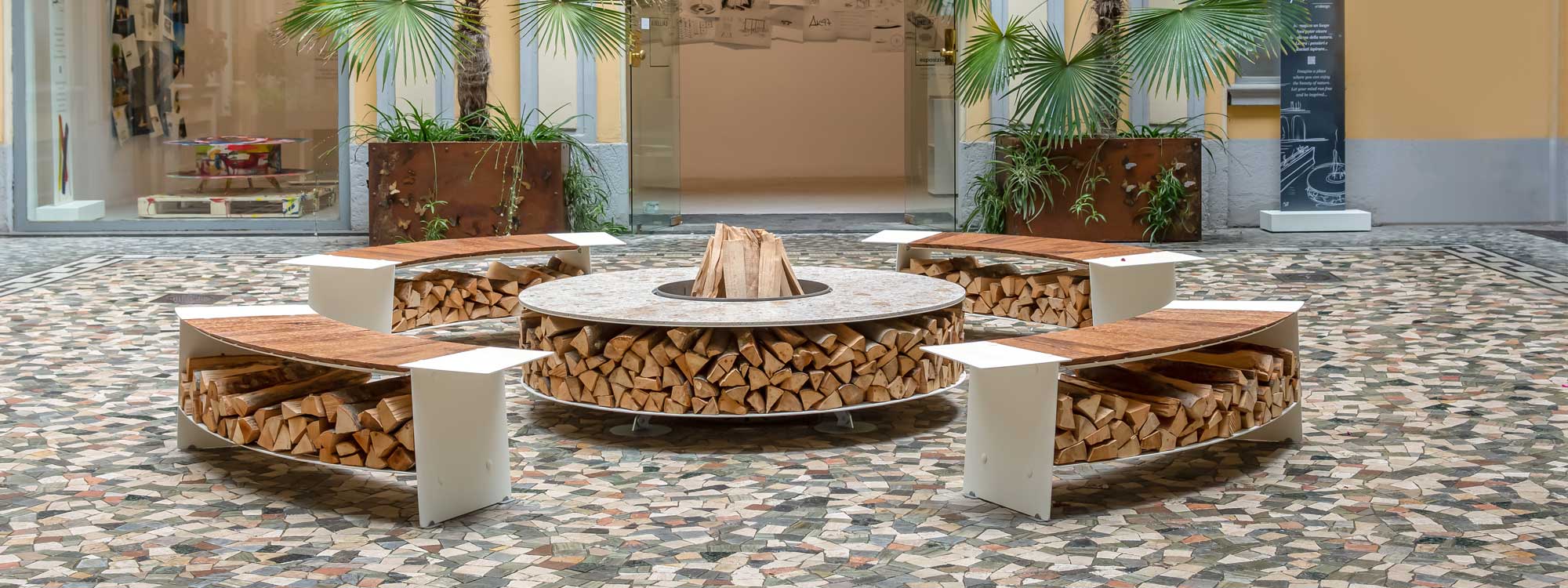 Image of AK47 Zero circular fire pit with Arlecchino ceramic upper surface, surrounded by Tobia modern bench seats in Italian courtyard
