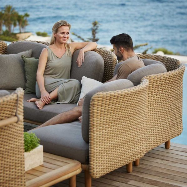 Image of couple relaxing on Cane-line Arch contemporary rattan corner sofa, shown on decking with water in the background