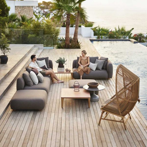 Image of couple relaxing on Capture modern garden sofa and Hive lounge chair, next to swimming pool with exotic plants in the background